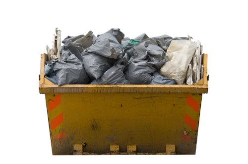 A large yellow commercial skip situated outdoors, filled to capacity with black and white rubbish bags made of plastic, some tightly knotted while others appear loosely gathered. The skip, which shows minor dirt and paint marks, is positioned on a paved surface that suggests an industrial or service area, possibly a driveway or waste collection zone. The bags contain a mix of waste materials; the black bags likely hold general rubbish, while the white bags may contain lighter, less dense waste. The background is plain white, emphasizing the skip and its contents without environmental context. The scene indicates a typical rubbish collection or disposal instance managed by Commercial Waste Tufnell Park, serving local businesses needing efficient waste management solutions in the area. Overall, the image captures the essential aspects of waste containment for commercial rubbish removal, highlighting the importance of proper waste packaging and disposal in a professional setting.